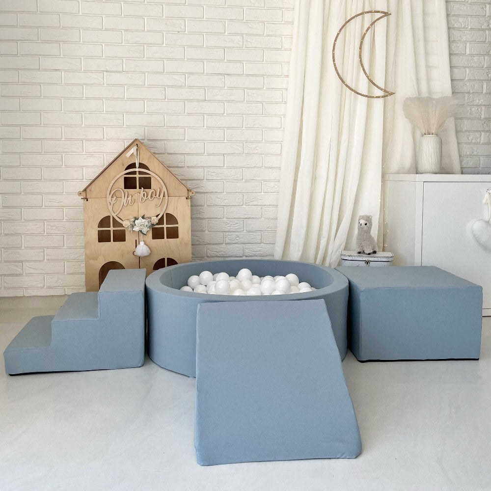 Blauw ballenbad met witte ballen, een trapje links, een helling vooraan en een kubusvormig blok rechts.