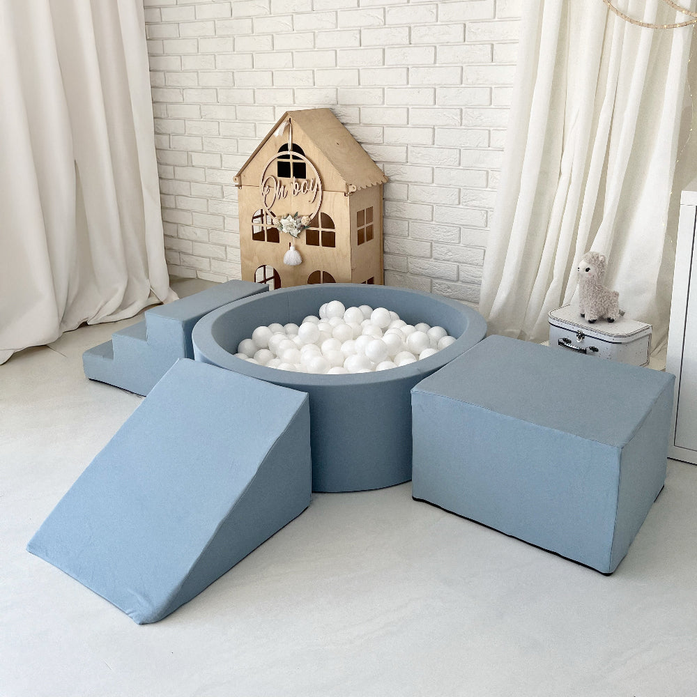 Blauw ballenbad met witte ballen en drie speelelementen, schuin van boven gezien: trapje, helling en kubusvormig blok.