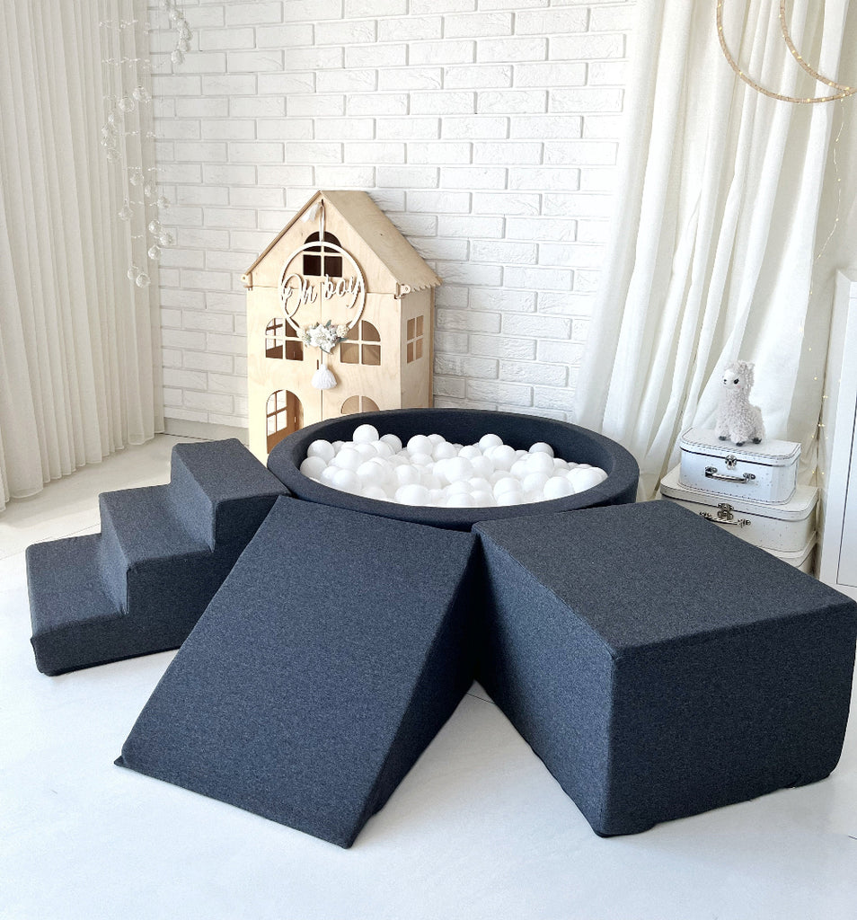 Grafietkleurig ballenbad met witte ballen, een trapje links, een helling vooraan en een kubus rechts in een speelkamer.