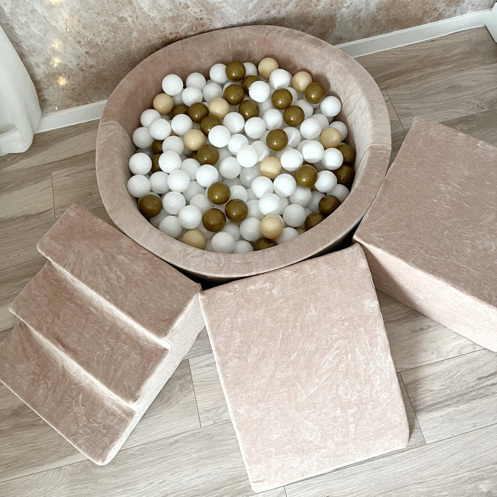Donkerbeige ballenbad van bovenaf met witte, beige en goudkleurige ballen, een trapje, helling en balk.
