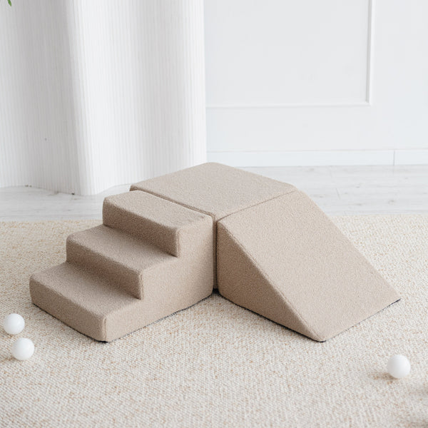 Beige bouclé speelset met trapje, blok en driehoek op een licht vloerkleed, met witte ballen eromheen.