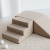 Beige bouclé speelset van dichtbij, met het trapje vooraan, het blok erachter en de driehoek rechts.