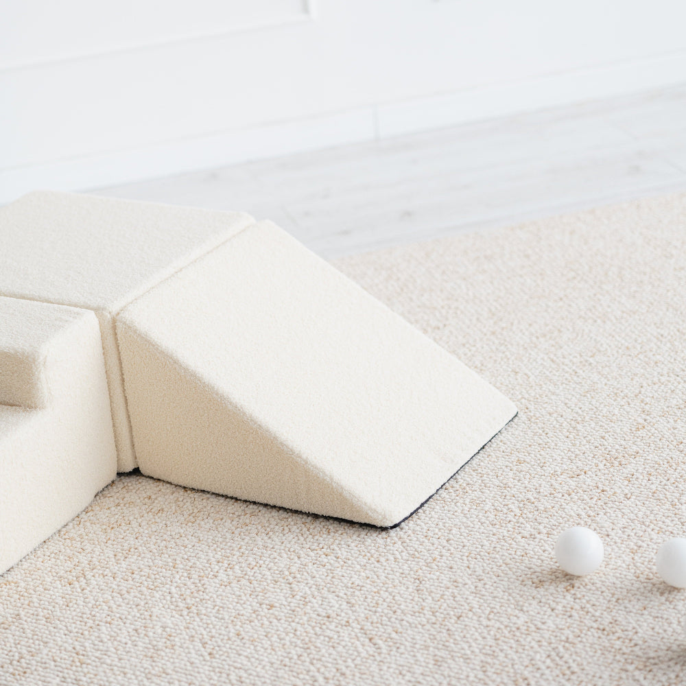 Detail van de crèmekleurige bouclé helling met een deel van het blok en trapje op een licht vloerkleed.