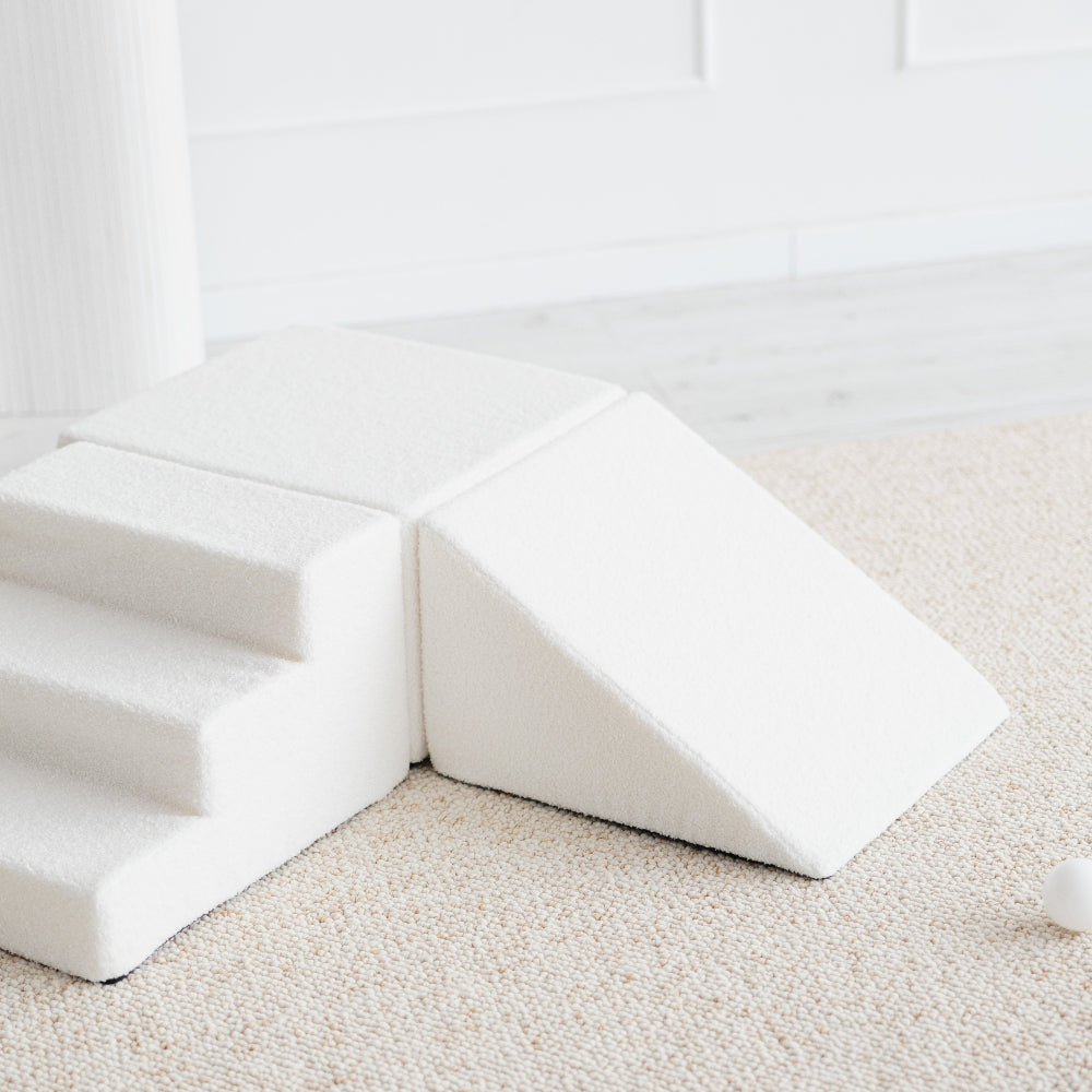 Detail van de witte bouclé speelset met een driehoekige helling rechts en een trapje links.