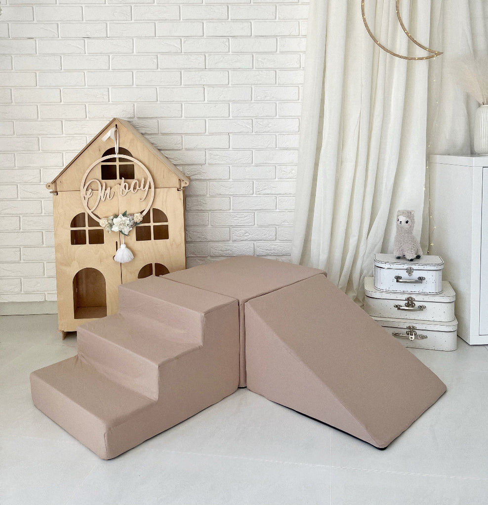 Beige speelset met drie elementen: een trapje, een rechthoekig blok en een helling in een kinderkamer.