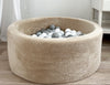 Rond beige teddy ballenbad met witte, lichtgrijze en donkergrijze balletjes op een houten vloer.