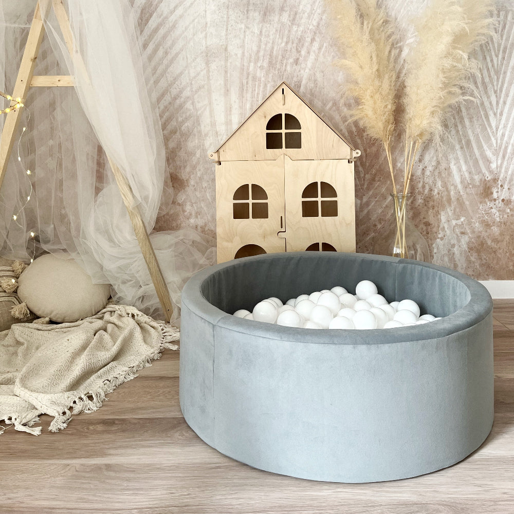 Rond grijs ballenbad met witte balletjes, van voren gezien in een speelhoek met een houten poppenhuis.