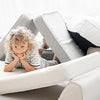 Kind ligt op de buik onder de driehoekig opgestelde segmenten van de beige bouclé lounger.