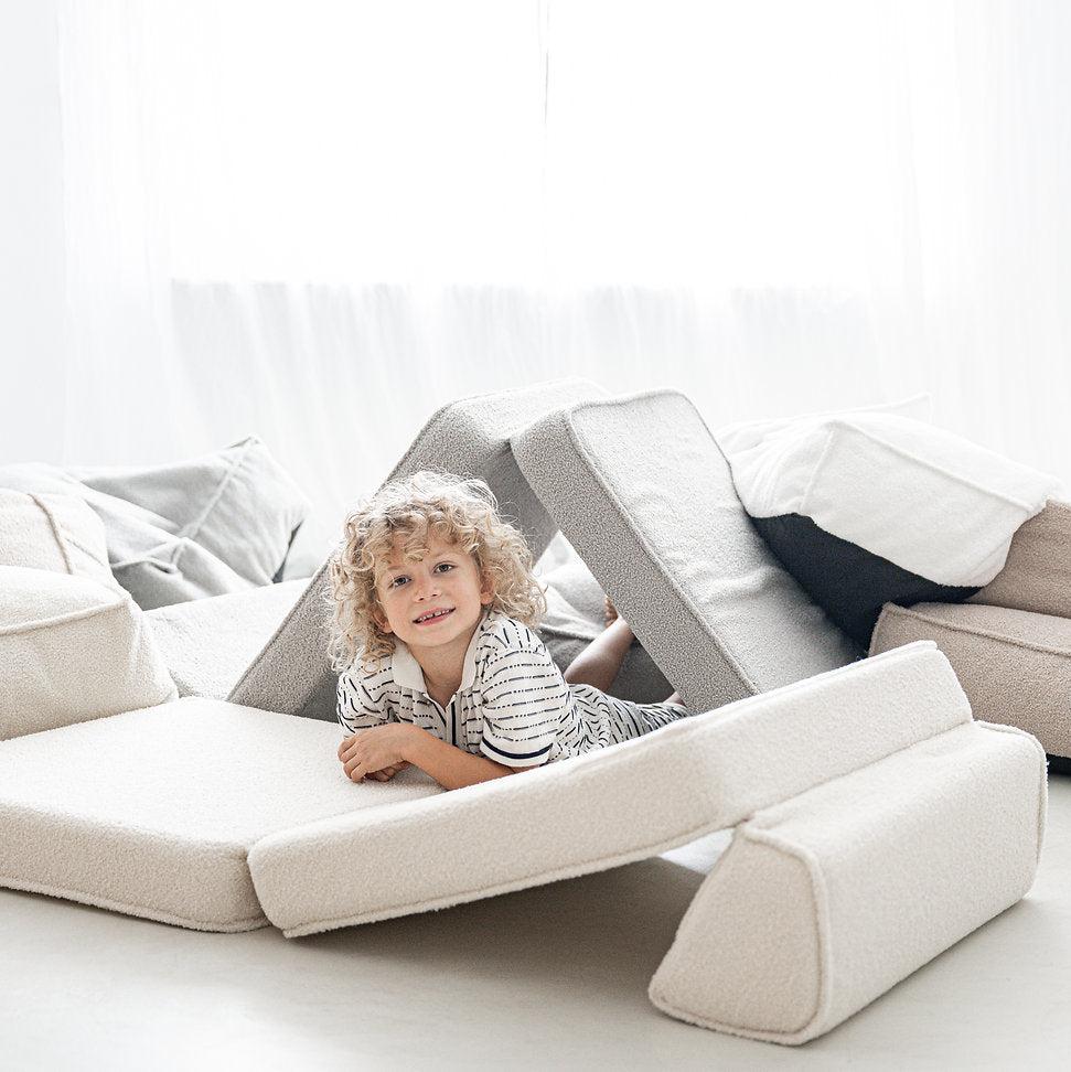 Kind speelt tussen de crèmekleurige bouclé segmenten van de lounger, opgesteld als tent.