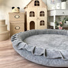 Grijs rond speelnest Soft Velvet met opstaande rand en ruches op een houten vloer in een kinderkamer.