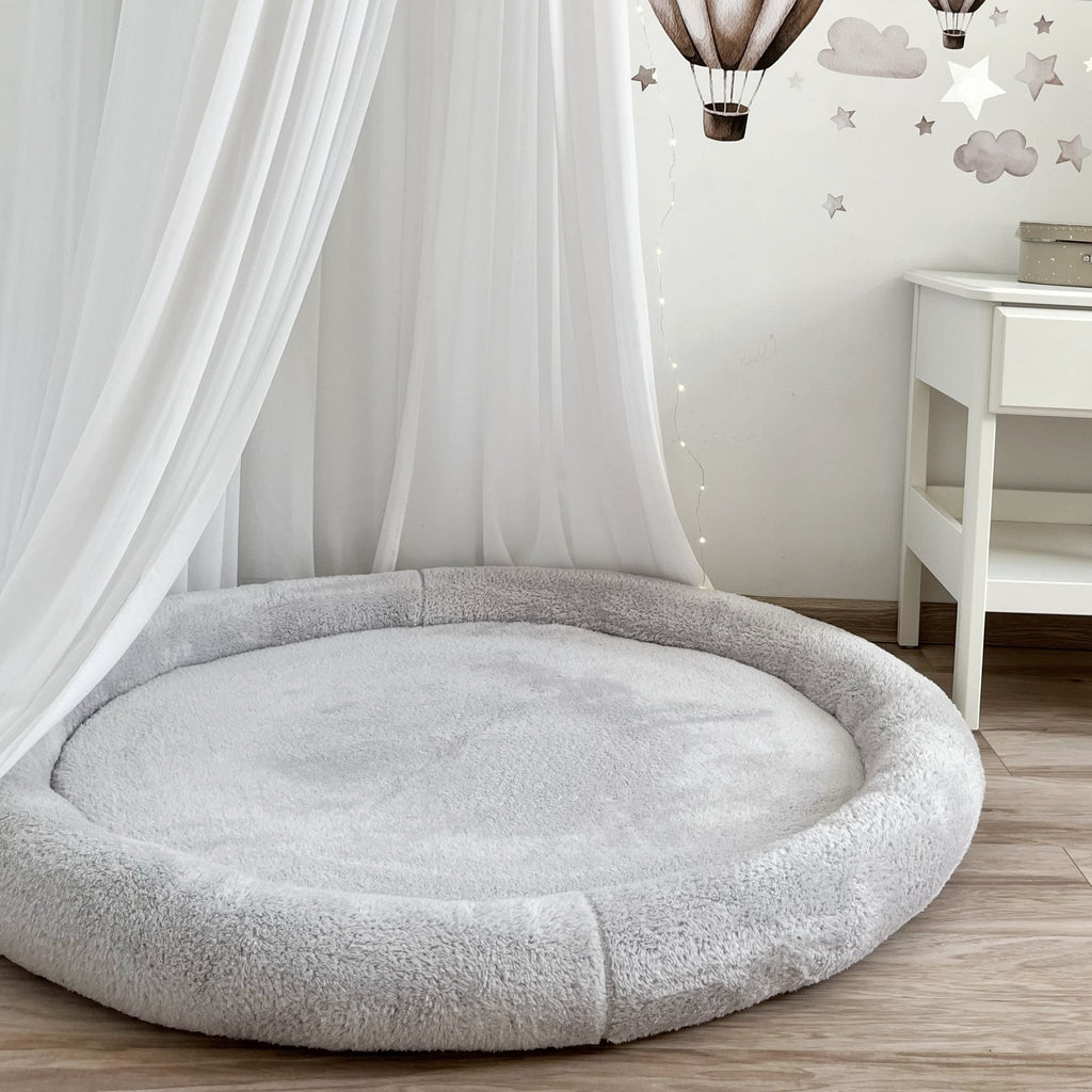 Grijs teddy speelnest met opstaande rand onder een witte sluier in een babykamer
