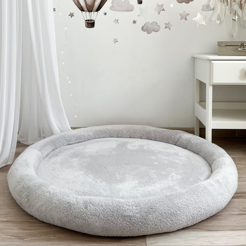 Grijs teddy speelnest met zachte opstaande rand, op een houten vloer onder muurdecoratie met wolken en sterren