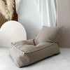 Beige bouclé zitzak met brede zitting en hoge rugleuning op een lichte vloer naast witte gordijnen.