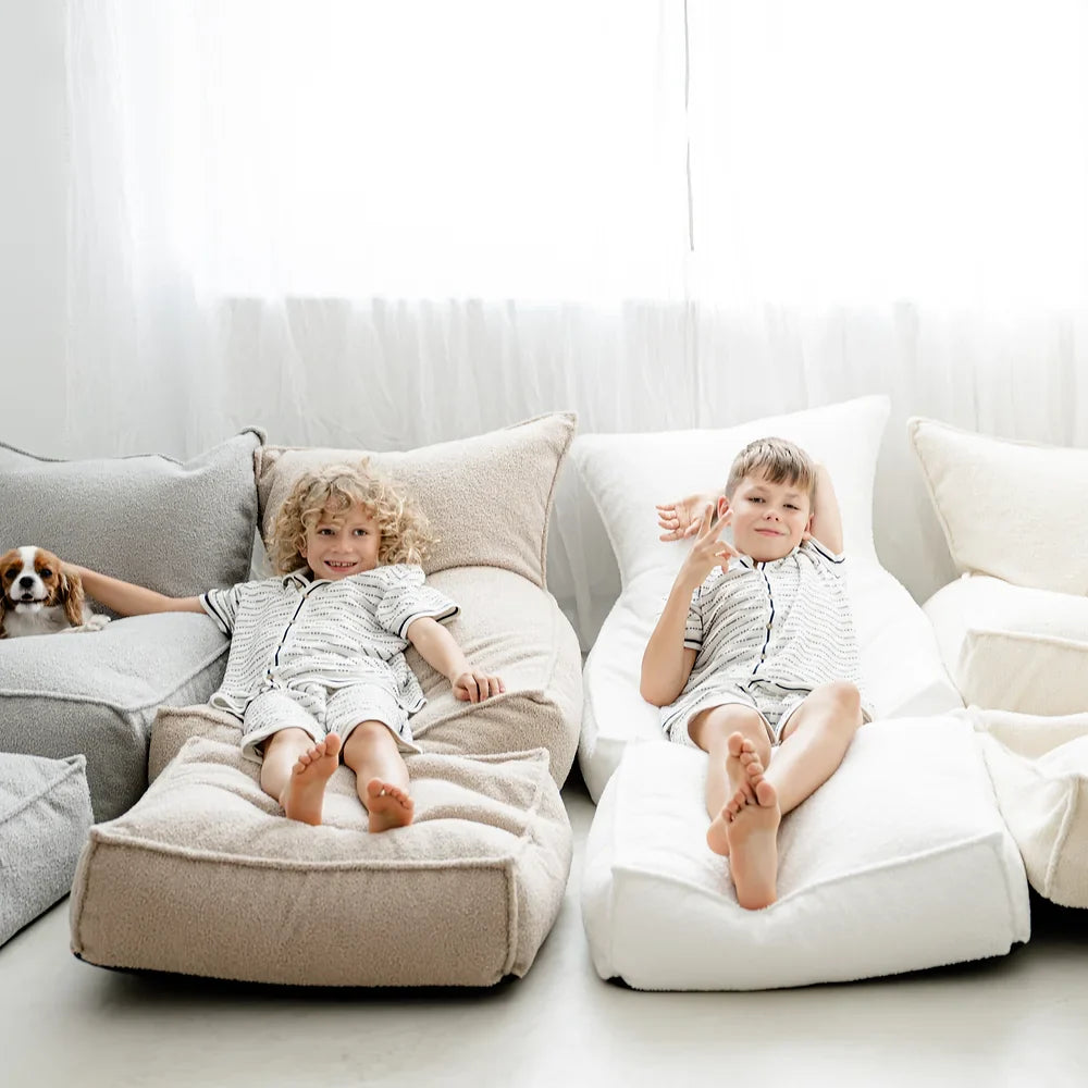 Twee kinderen liggen naast elkaar op een beige en een crèmekleurige bouclé zitzak.